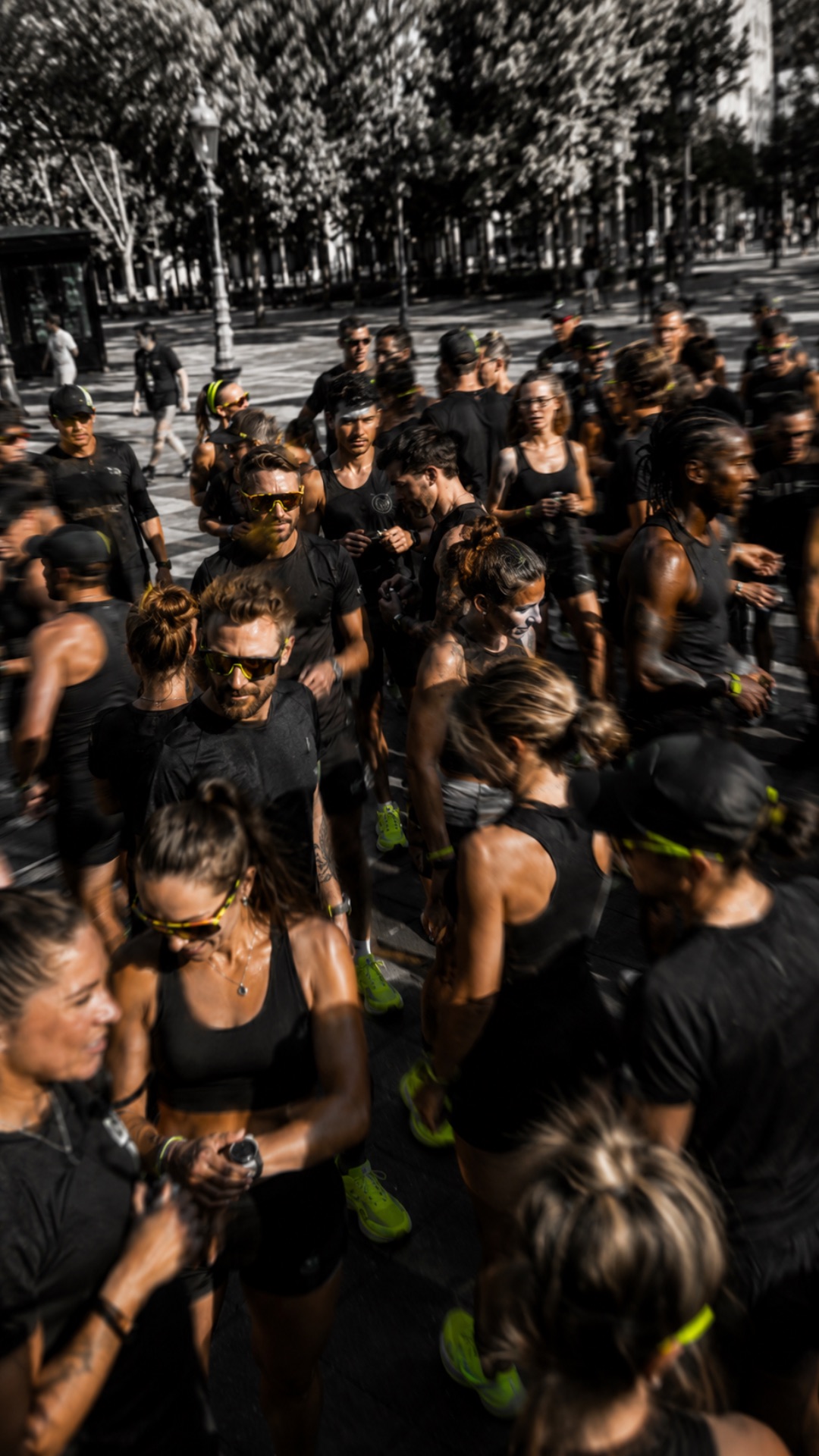 Des dizaines de coureurs en noir massés sur une allée arborée, à l’instant du départ.